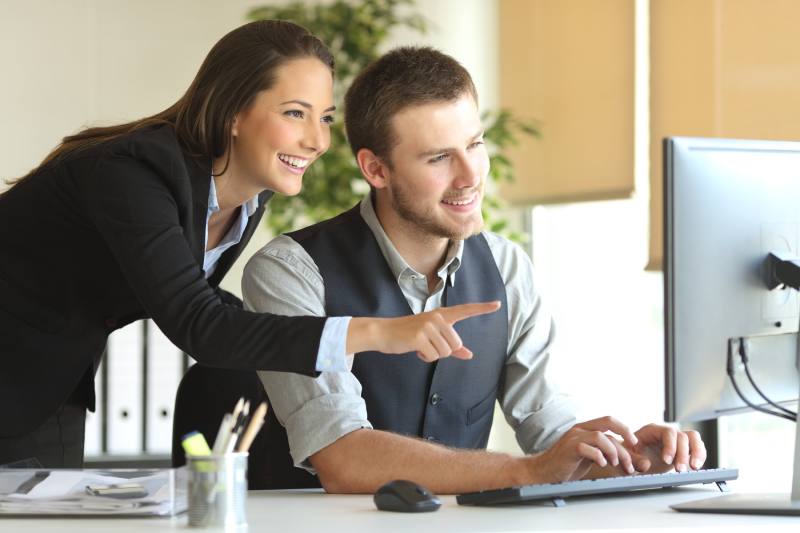 Coworkers working on line with a desktop computer in a desktop at office with a window in the background