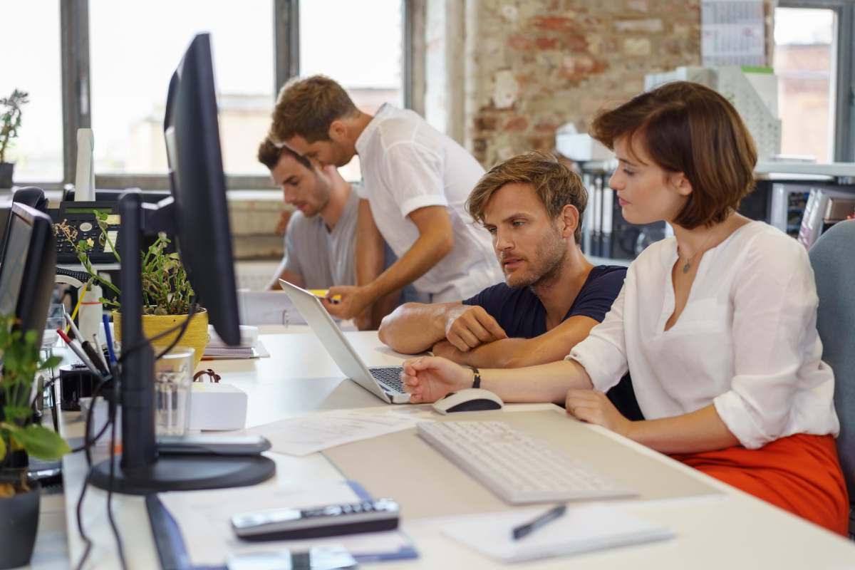 Side view of young people colleagues wearing casual at desk with computers and papers working together in coworking office