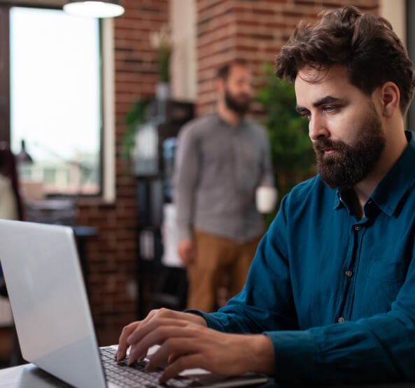 entrepreneur-man-sitting-desk-startup-office-brainstorming-ideas-while-working-marketing-project-analyzing-company-turnover-laptop-diverse-businesspeople-planning-business-collaboration 1